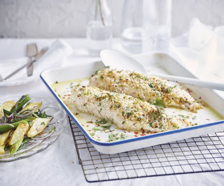 Roodbaars met een crumble van gember, sesam en chili met aardappelsalade De gegrilde roodbaars uit de oven ligt op een witte bakplaat en staat op een rooster. De crumble zorgt voor een zomerse sfeer in het gerecht. Naast de ovenschaal staat een bordje met wat aardappelsalade uitgeschept.