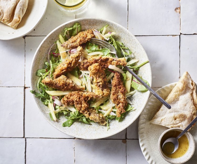 Salade met krokante leverreepjes en mosterddressing Er staat een diep bord op het aanrecht, gevuld met meerdere slasoorten en krokant gebakken leverreepjes. De mosterdressing staat er langs om zelf toe te voegen.
