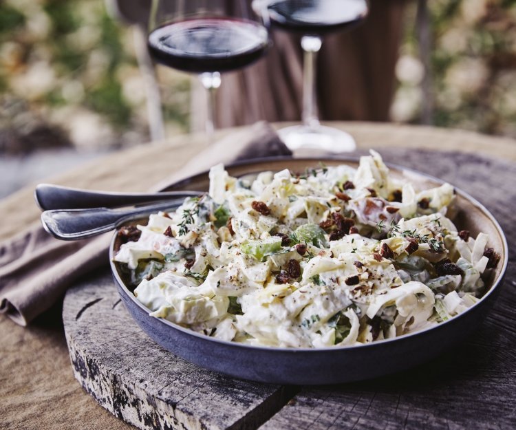 Salade van witloof, appel, selder en rozijnen Een witloofsalade met yoghurtdressing, selder, rozijnen, appel en gember. Echt eentje om duimen en vingers van af te likken. De salade is geserveerd in een groot diep bord en staat op een boomstronkschijf.