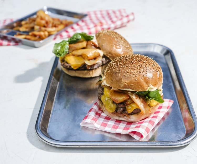 Twee hamburgers liggen op een inoxe plateau. De ene burger moet zijn hoedje nog krijgen.