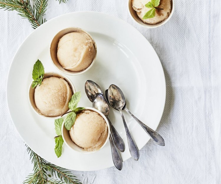 Sorbet van peer en citroen Drie sorbets staan op een wit rond bord, afgewerkt met een muntblaadje. De koffielepeltjes liggen ook op het witte bord, de tafel is aangekleed met takjes kerstboom.