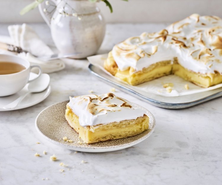 Taart van croissants, lemon curd en meringue Croissanttaart staat aangesneden op tafel, thee is opgediend en bordjes staan klaar. De meringue is mooi gekleurd door de brulébrander.
