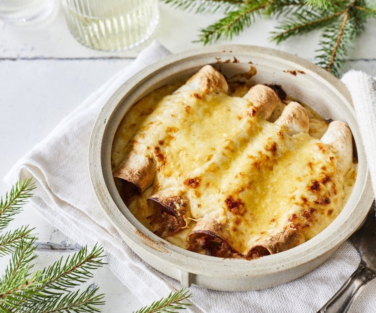 Opgerolde wraps gevuld met traagggegaard vlees liggen netjes naast elkaar in een ovenschotel. Hierover is kaassaus geserverveerd en even gegrild. Perfecte snack als bijgerechtje op je feesttafel, heerlijk voor groot en klein. 