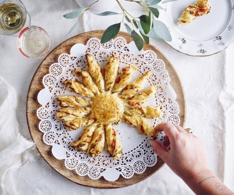 Tarte soleil met ricotta van berloumi en kerstomaat Een bladerdeeghapje met ricottakaas van bij ons en kerstomaatjes. Dit hapje is speciaal door de vorm, hij is nl gemaakt in de vorm van een zon. Hij ligt op een houten dienblad en er neemt een hand een zonnestraal om op te proeven.