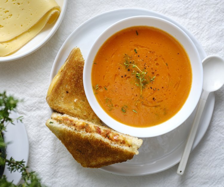 Tomatensoep van geroosterde tomaten met kaastoast Een heerlijke kom soep staat klaar op tafel in een wit kommetje. Wij serveren hem met een toast van kaas en tomaatjes. Een heerlijke en voedzame lunch.