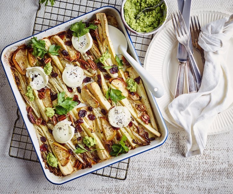 Traybake met witloof, pastinaak, appel en geitenkaas Op een rooster staat een ovenschaal met hierin de langgesneden witloofstronkjes, pastinaak en partjes appel. Hieop liggen de schijfjes geitenkaas die ligtjes wegsmelten. Er liggen enkele toefjes erwtendip op voor de afwerking en extra smaak.
