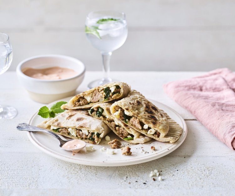 De turkse pannenkoek gevuld met gehakt, spinazie en feta ligt op een wit bord. Er ligt een roze servette langs en het chili-dipsausje staat bovenaan. 