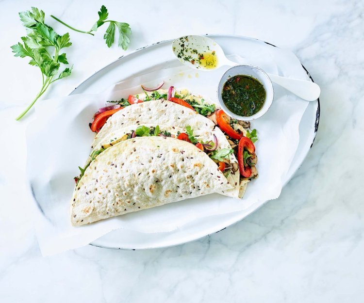 Vegetarische quesadilla met geroosterde knolselder, champignons, paprika en Brugge Oud Vegetarische quesadilla gevuld met geroosterde knolselder, champignons, paprika en Brugge Oud. 2 stuks liggen gepresenteerd op een ovaal wit bord, samen met de vinaigrette in een potje apart. Takje verse koriander ligt er langs voor extra groen en sfeer aan het beeld mee te geven.