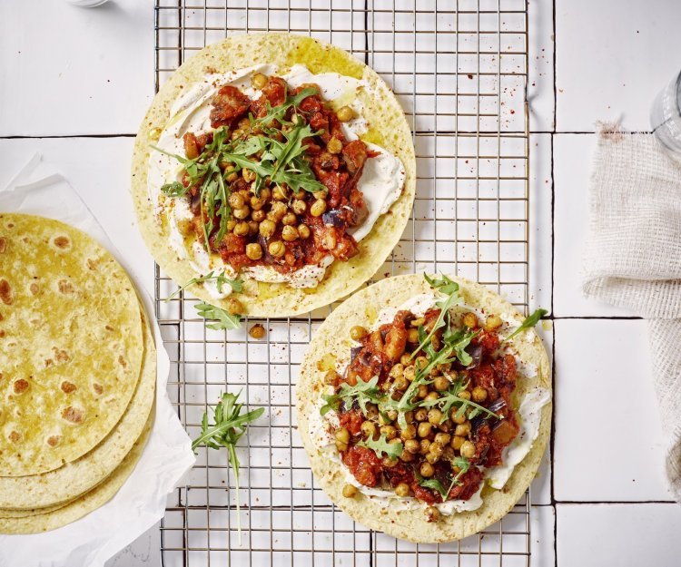 Wrap met roomkaas, geroosterde kikkererwten en een spread van aubergine en tomaten Twee wraps liggen op een ovenrooster klaargemaakt. Ze zijn belegd met roomkaas, tomatenspread en geroosterde kikkererwten. Er liggen nog enkele extra wraps langs. Het gerechtje is afgewerkt met enkele blaadjes rucola.