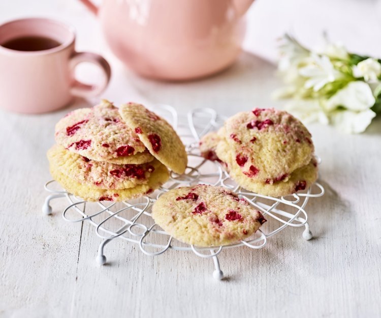 Zandkoekjes met frambozen Op een kleine taartrooster liggen enkele koekjes te drogen. De koekjes hebben rode vlekjes van de framboosjes. Er staat een theepot langs met al een uitgeschonken thee in bijpassende roze tas.