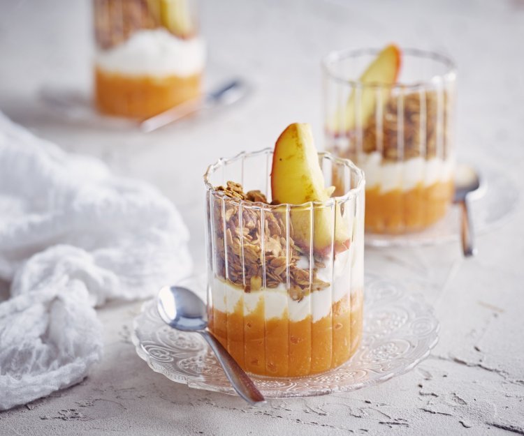 Zoete aardappel met kwark, granola en appel Op tafel staan 3 glaasjes gevuld met dit ontbijtje. Onderaan ligt een lepeltje zoete aardappel, hierbovenop de kwark, granola en een stukje gestoofd appel. De kleuren van dit ontbijtglaasje zijn gewoon om blij van te worden.