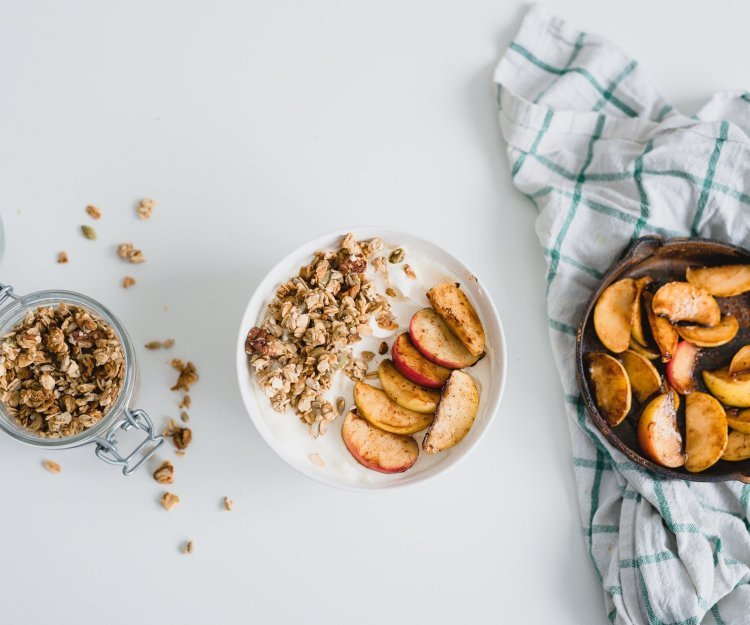 Yoghurt met granola en gebakken appeltjes Op tafel staat een ontbijtkommetje gevuld met yoghurt, granola en lauwwarme appeltjes.