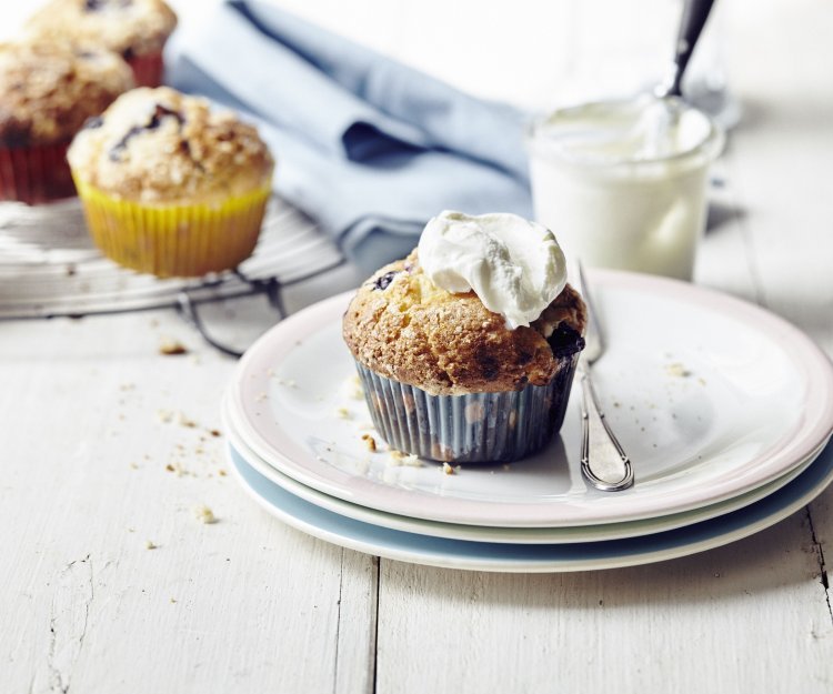 Er staan meerdere muffins op de tafel en eentje op een bordje dat al is afgewerkt met witte topping van slagroom of zure room.