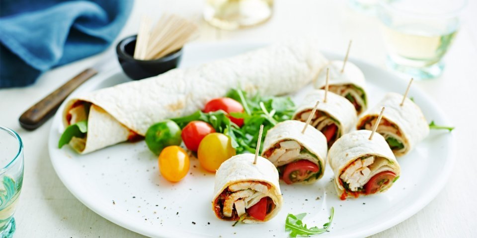 Op een bord ligt een rol wrap met groenten, wat kerstomaten en zes stukken wrap met een prikker in. Op een bord ligt een rol wrap met groenten, wat kerstomaten en zes stukken wrap met een prikker in.