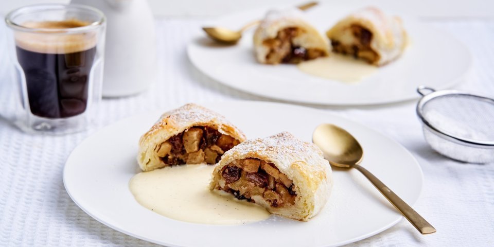 Apfelstrudel met vanillesaus Op tafel staan twee bordjes met een hemels lekker dessert. Dit keer een appelstrudel of apfelstrudel zoals de echte, met een portie vanillesaus. Een koffie mag niet ontbreken.