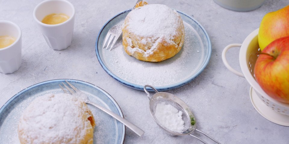 Appelbollen Heerlijke appelbollen staan klaar op tafel om toe te happen. Er staan twee kopjes kofie vij en verse jonagold appelen. De appelbollen zijn bestrooid met bloemsuiker.