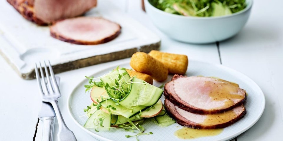 Ardeens gebraad met mosterdsaus, oude Geuze en een salade van appel en komkommer Op een houten witte tafel staat een portie klaar. Een wit bord gevuld met twee sneetjes van het varkensgebraad, kroketten en de salade van komkommer met appel.