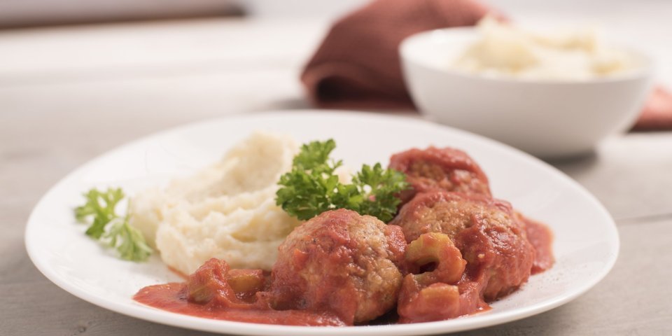Balletjes in tomatensaus Eén portie balletjes in tomatensaus met puree, komt eraan. Hij staat klaar op een houten tafel, klaar om op te eten.