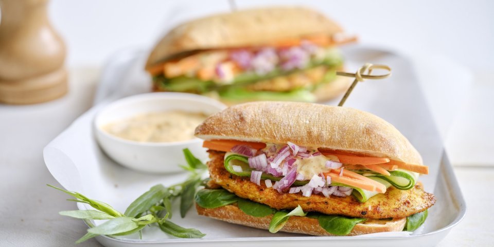 Belegd broodje met gegrilde kip Een belegd broodje ligt op een bordje. Hij is belegd met een stukje gebakken kipfilet, verse wortel, komkommer en een sausje. De resterende saus werd in een klein potje erbij geserveerd.
