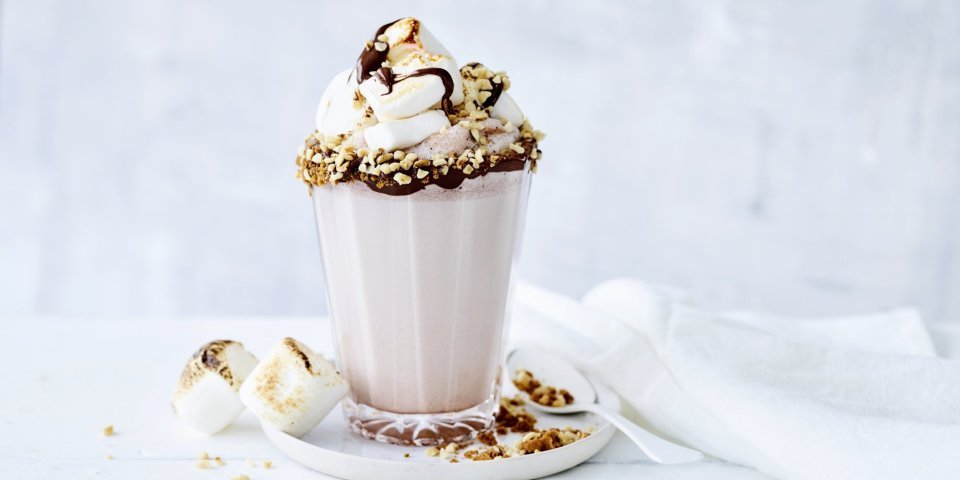 Een chocolademilkshake staat te shinen in het midden van de foto. Hij is afgewerkt met geroosterde marshmallows en vers gesmolten chocolade. Crazy shake ten top!