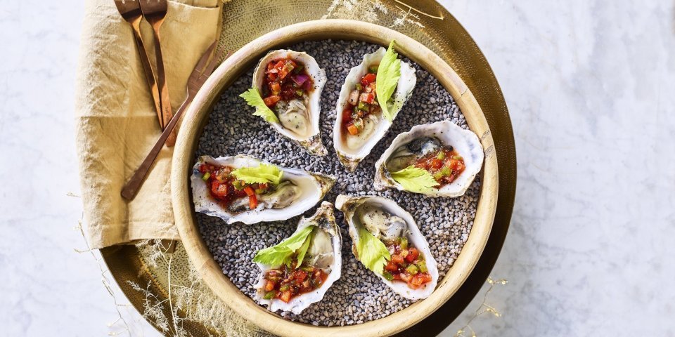 Bloody Mary oesters Zes oesters liggen te schitteren op de feesttafel. Ze zijn voor de helft gevuld met de vinaigrette op basis van tomatensap, stukjes paprika's en vodka. Afgewerkt met een blaadje selder die zorgt voor de frisgroene kleur bij de rode topping.