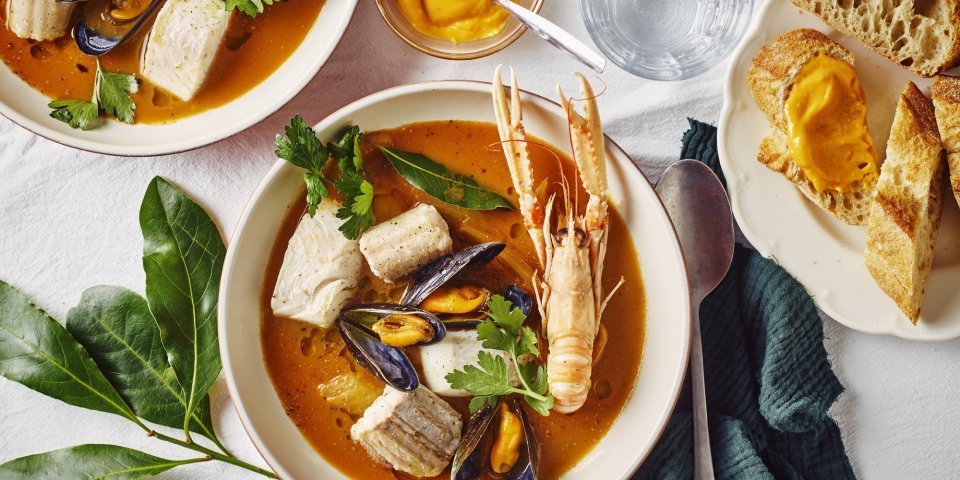 Bouillabaisse belgique Een heerlijk kleurrijk bordje bouillabaisse staat op tafel. Wij maakten hem met topproducten van hier. Er ligt een donker groene linnen servette langs en bordje stukjes brood en verse rouille.