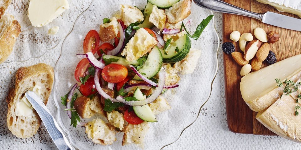 Een glazen schaaltje, ovaalvormig, gevuld met knapperige croutons, tomatenstukjes en komkommermaantjes.  