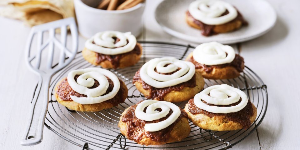 Cinnamon rolls-koekjes Op een taartrooster liggen 6 koekjes af te koelen. Het zijn koekjes van cinnamon rolls, een nieuwe versie om te genieten van deze heerlijke en kruidige zoetigheid. Op de koekjes is frosting gespoten op basis van roomkaas.