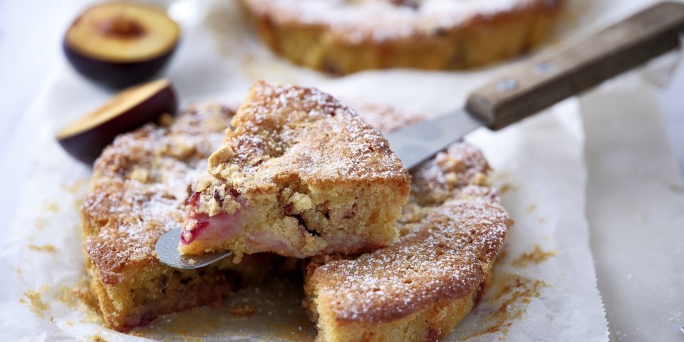 Crumble-taart met pruimen Er liggen twee crumbletaartjes klaargemaakt op het aanrecht. Er is al eentje aangesneden om meteen te proeven.