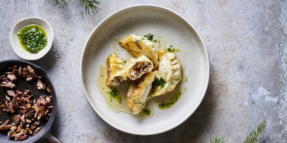 Dumplings met boschampignons en spek Dumplings liggen op een beige bordje, er werd een dumpling opengesneden. Zo krijg je een kijkje in de vulling op basis van boschampignons en gerookt spek.