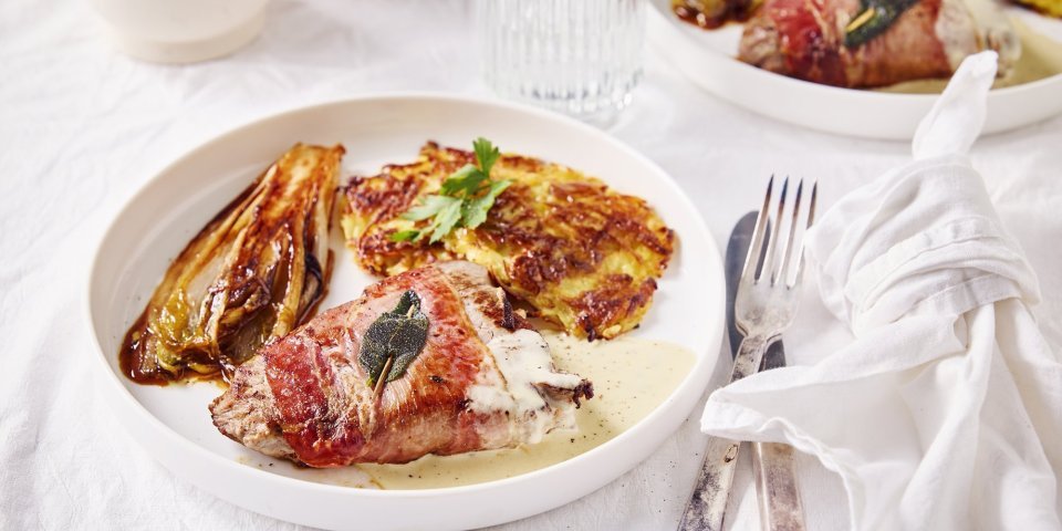 Er staat een mooi groot wit bord op de tafel. Hierin ligt een homemade rosti, een stronkje witloof en saltimbocca van filet mignon. Afwerken doen we met een roomsasusje van blauwe kaas.
