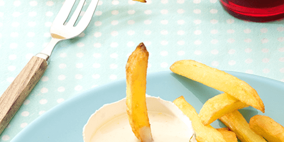 Zelfgemaakte mayonaise op een blauw bord staat een potje gevuld met mayonaise om je frietjes in te dippen.
