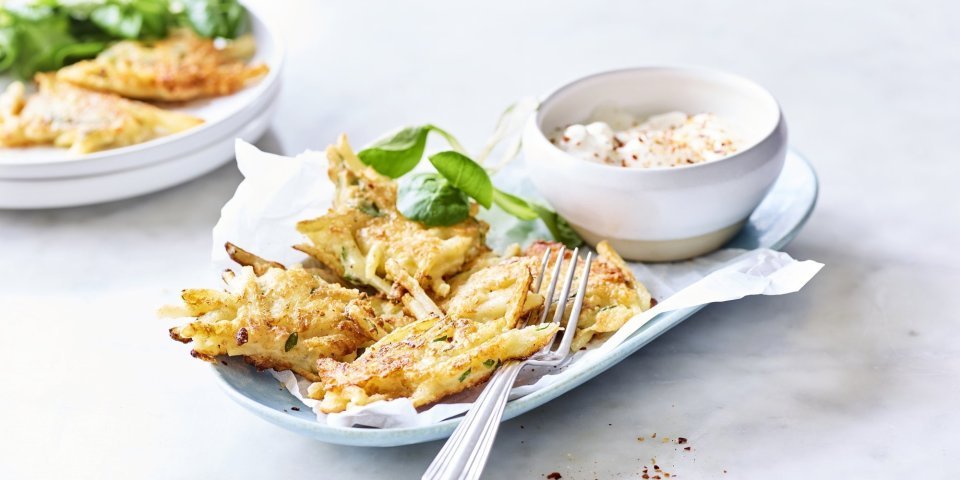 Meerdere fritters liggen op een licht blauw bordje vergezeld van een blaadje veldsla en het dipsausje op basis van yoghurt en specerijen.