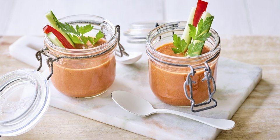 Twee bokaaltjes met gazpacho staan op een marmer plankje, een ideaal alternatief voor te weinig glazen. We gaven de gazpacho een feestlook met staafjes komkommer en paparika in het bokaaltje te laten op springen.  