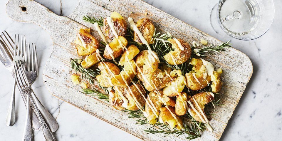 Eens een patatje in een feestjas op tafel? Serveer deze ovenaardappeltjes en ontvang veel "mmmmm-lekker complimentjes". Deze gecrushte aardappeltjes zijn geserveerd op een houten plank met een heerlijk picklessausje.  