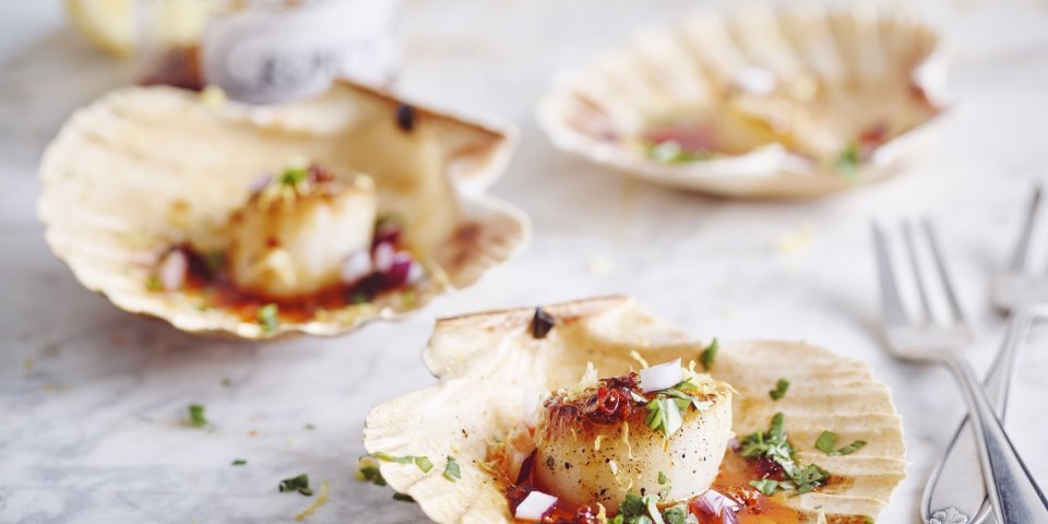 Gegrilde Sint-jackobsnoten met chili 3 Sint-jackobsschelpen liggen open op het aanrecht met hierin de krokant gegrilde jackobsnoten en afgewerkt met de crispy chili olie.