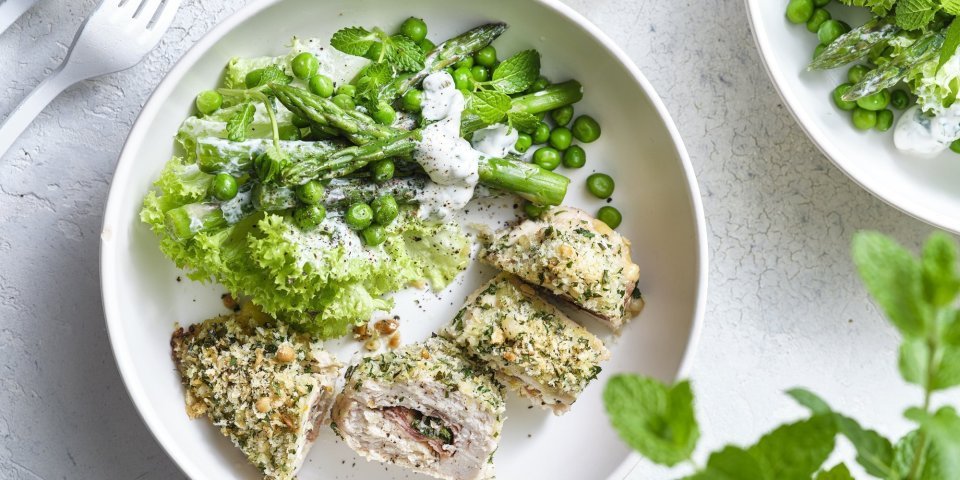 Gegrilde kipfilets met crumble en groene salade Hier wil ik meteen aan beginnen. De kipfilet is gevuld met basilicum, plakje kaas en ham. Daarna kreeg hij een flinke laag pako over zich heen en ging hij de oven in. Wij combineren deze krokante gegrilde kipfilet met een groene salade op basis van krulsla, erwtjes, groene asperges en verse munt. Dit gerechtje is opgediend in een wit bord om de groene kleur extra pit te geven.