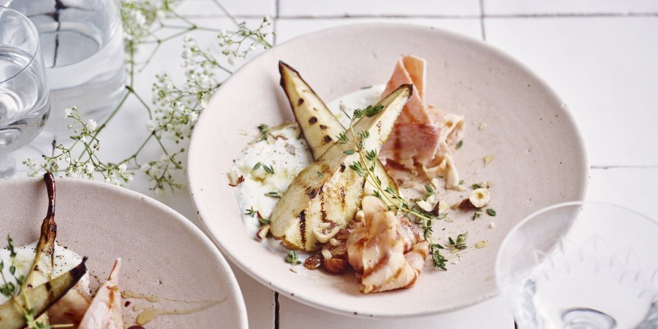 Gegrilde peer met ham, verse kaas en tijm Een heerlijk fris bordje met gegrilde partjes peer op een schep verse plattekaas met tijm, honing en Meesterlyck-ham.