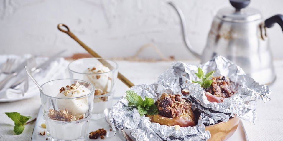 Gepofte appel met crumble van speculoos en vanilleijs Een vers gepofte appel vanop de bbq ligt in een klein pannetje op een dienblad vergezeld met een glaasje vanilleijs en verse koffie.