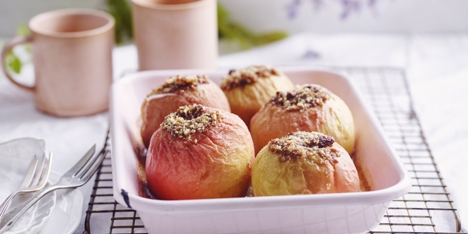 Gevulde appels in een licht roze ovenschaal. Achteraan staan twee roze kopjes, klaar om aan het ontbijt te beginnen.