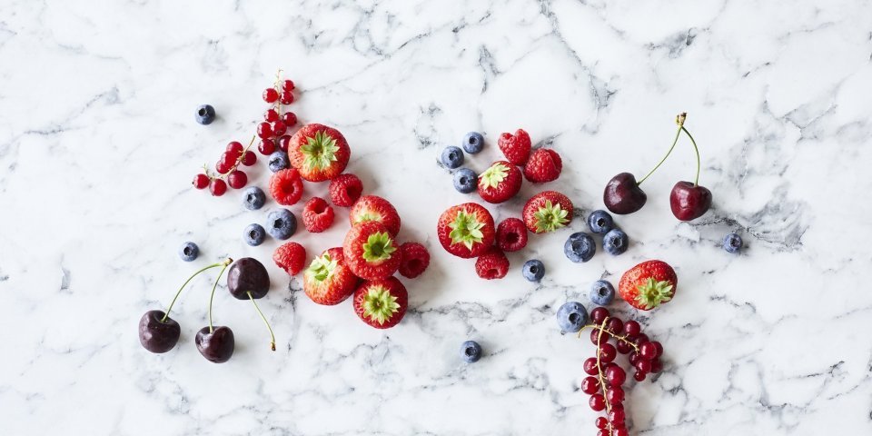 Aardbeien, frambozen, blauwe bessen, rode bessen en kersen liggen op een marmer aanrecht. Klaar om te verwerken in een homemade confituur. 