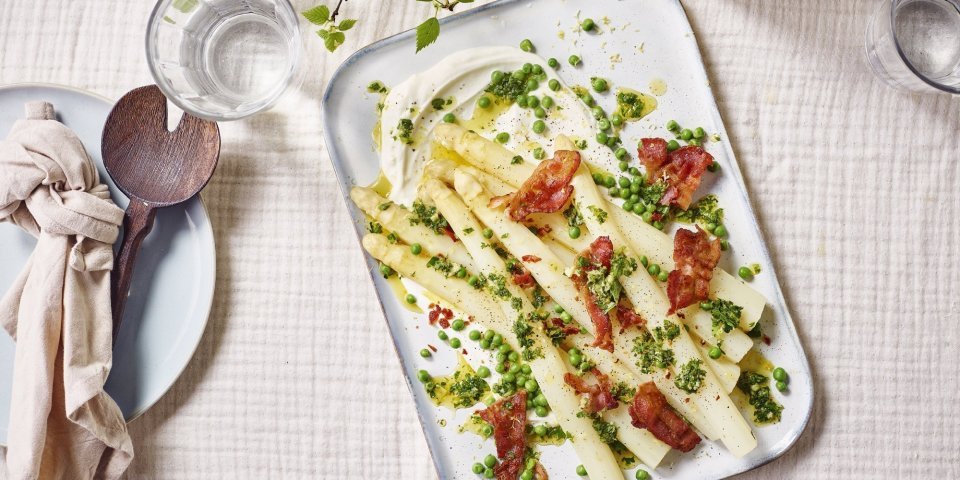Hangop met asperge, erwtjes en spek Op tafel staat een groot rechthoekig bord met hierop het bijgerecht geserveerd. Het is een pareltje om naar te kijken, terwijl dit makkelijk en simpel te maken is.
