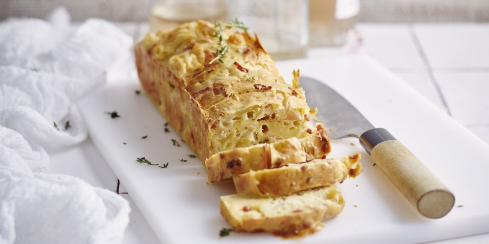 Hartige cake met appel, Brugse kaas en spek Een cake die niet zoet is, maar hartig. Wij maakte hem met appel, kazen van bij ons en spekjes... heerlijk! Hij ligt aangesneden op een witte snijplank en werd afgewerkt met verse tijmblaadjes.