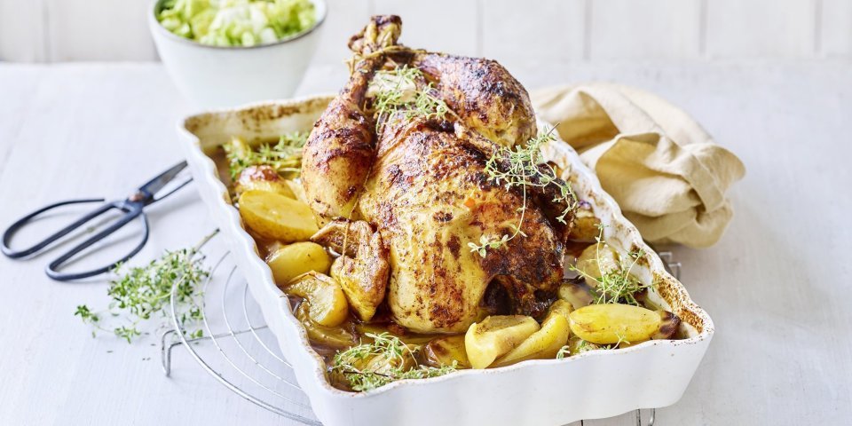 Hoevekip uit de oven met appeltjes en krieltjes De gebraden kip ligt te blinken in een ovenschaal met krieltjes en appeltjes naast. Het gerechtje is afgewerkt met groene verse tijmtakjes, het zwarte schaartje waarmee de kruiden werden afgeknipt ligt er langs.