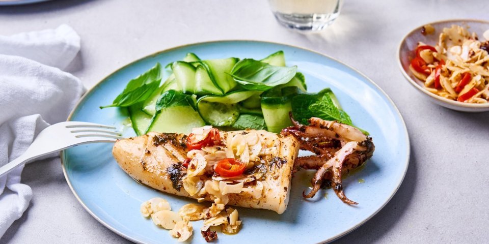 Inktvis met crunchy amandelen en slaatje van komkommer en kruiden Op een lichtblauw bordje ligt een gegrilde inktvis met amandelen te blinken. Wij serveren hem met een slaatje op basis van komkommer, munt en basilicum.