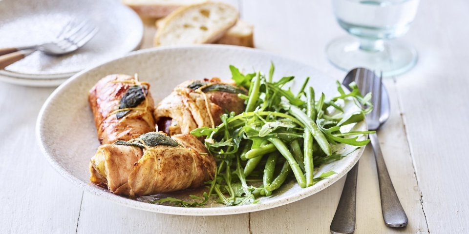 Involtini met peer en geitenkaas Heerlijke kalfsrolletjes liggen in een diep bord met de boontjessalade er naast. De vleesrolletjes zijn gevuld met peer en geitenkaas. Er staat een glas water langs en wat stukjes brood.
