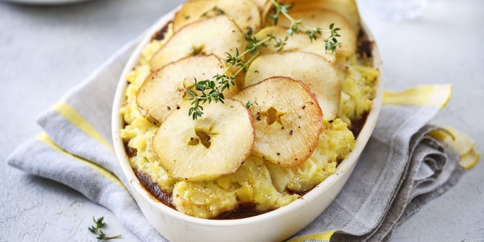 Jachtschotel met schijfjes appel Op tafel staat een ovale witte ovenschotel gevuld met onderaan het stoofpotje, hierop de aardappelpuree en tenslotte de appelschijfjes. Dit geeft een mooi beeld, niet alleen om naar te kijken ook om meteen te beginnen eten. Het gerechtje werd afgewerkt met verse takjes tijm.