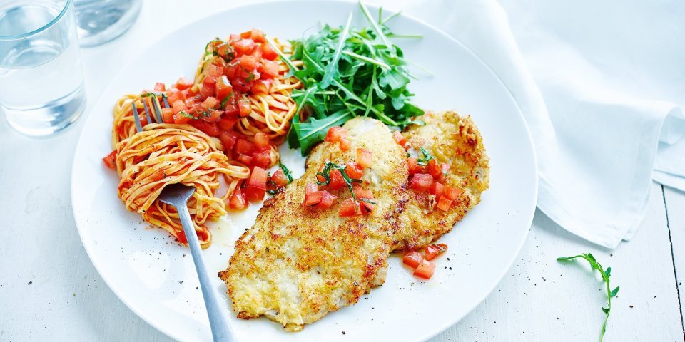 Kalfslapjes alla Milanese met tomatensalsa Op tafel staat een portie van de krokante kalfslapjes alla Milanese met tomatensalsa, pasta en rucola.