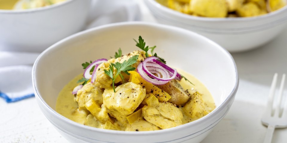 Kip curry met krieltjes Op tafel staan twee porties uitgeschept, om onmiddelijk aan te vallen met mes en vork. De curry kleurt mooi goudgeel, terwijl de rode ui voor contrast zorgt. We werken af met een takje verse peterselie voor extra kleur.