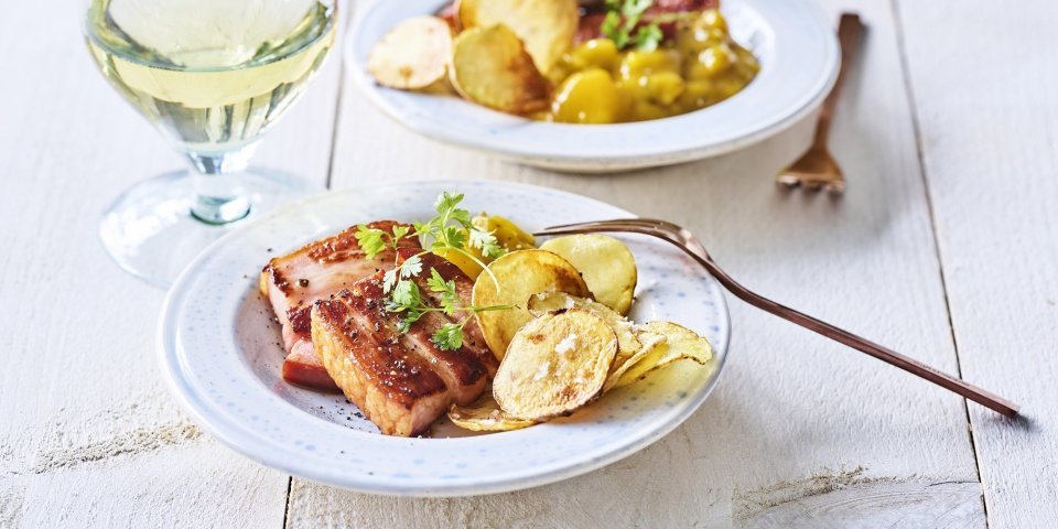 Krokant buikspek met homemade chips en Belgische pickles Er staan twee bordjes op tafel gevuld met krokant buikspek, krokante aardappelchips en een schep Belgische pickles. Een voorgerechtje boordevol Belgische topproducten!